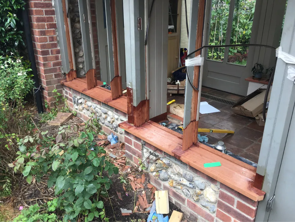 Partially installed wooden window frames on a brick and stone wall with tools and materials around.