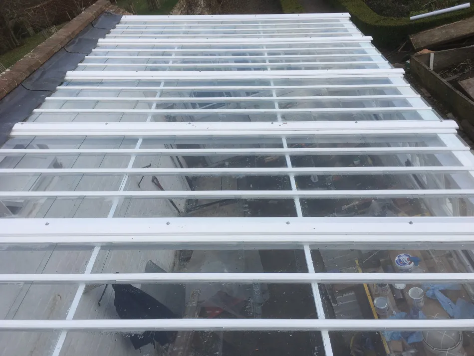 View looking down through a transparent glass roof with white support beams over a cluttered workshop area.
