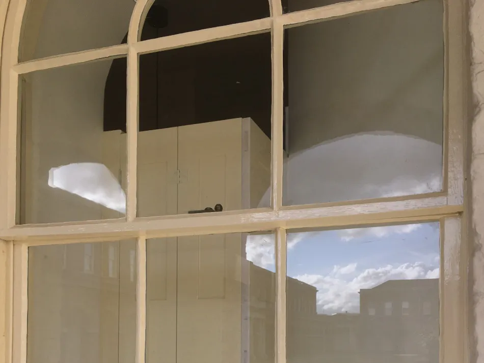 Reflection of a blue sky with clouds and building silhouettes on a cream-colored window with multiple panes.