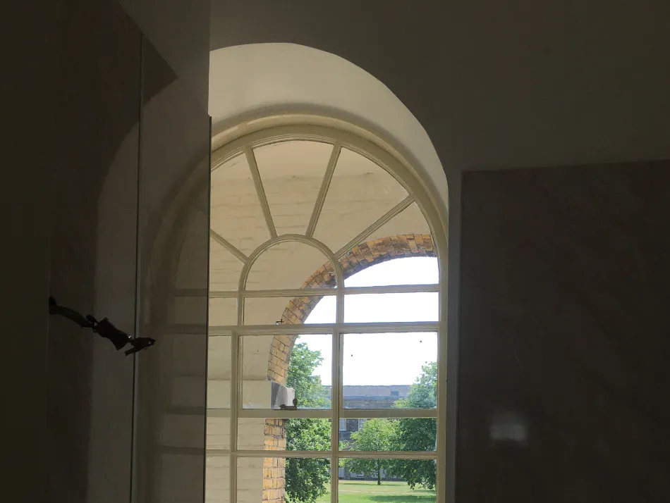 View through an arched window with white framing showing trees and a grassy area outside.