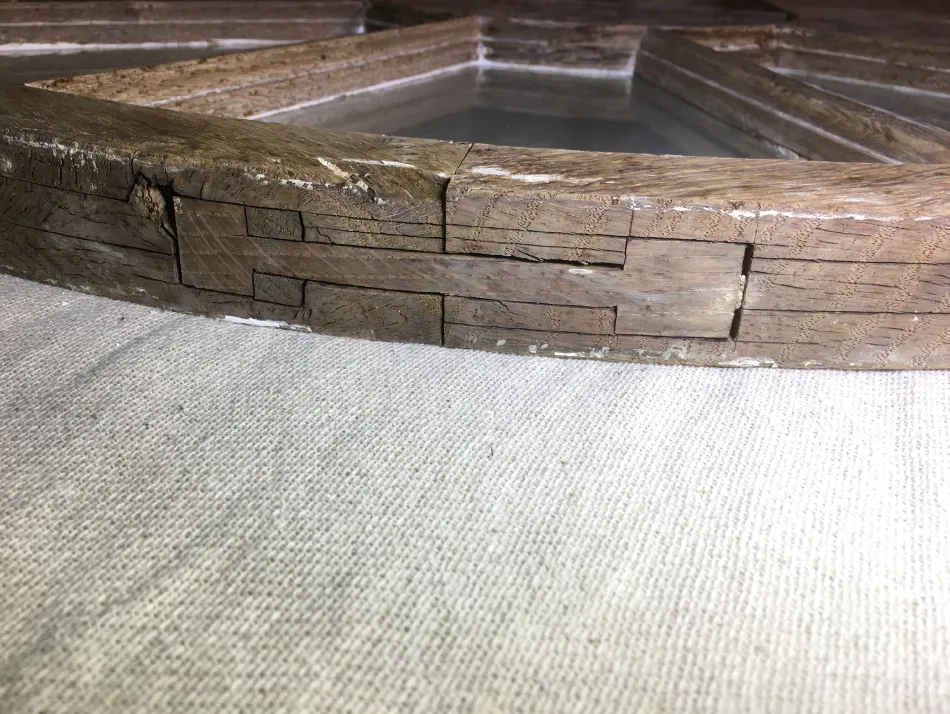Close-up of an aged wooden frame with intricate joint construction resting on a textured white fabric surface.