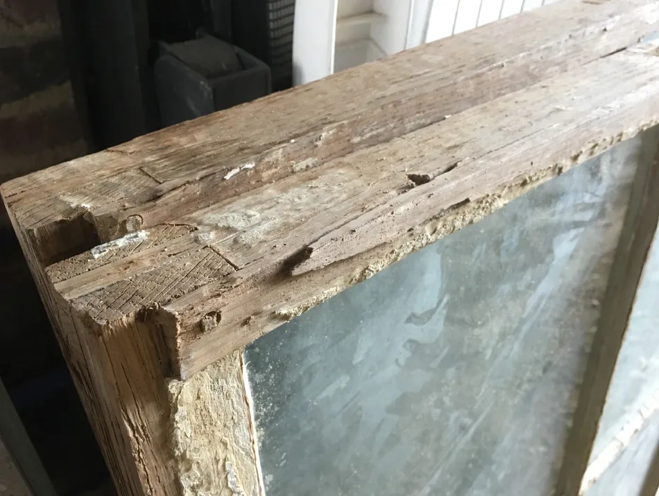 Close-up of an old wooden window frame with weathered paint and textured glass pane.
