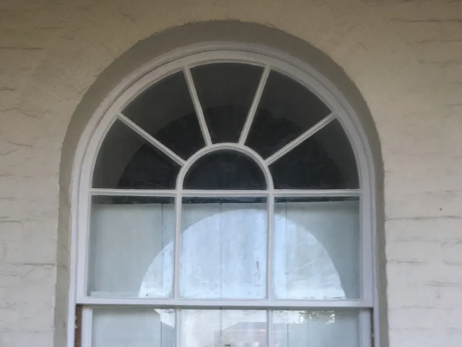 Arched window with white trim and divided panes set in a textured light-colored wall.