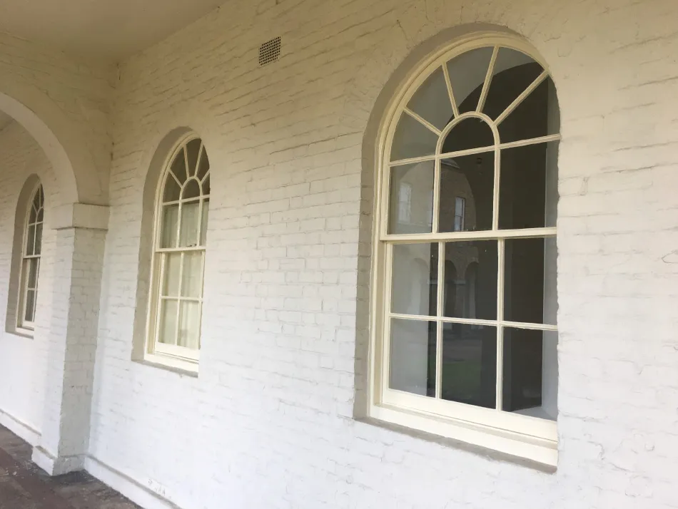 Three arched windows with decorative grid patterns on a white painted brick wall with archways.