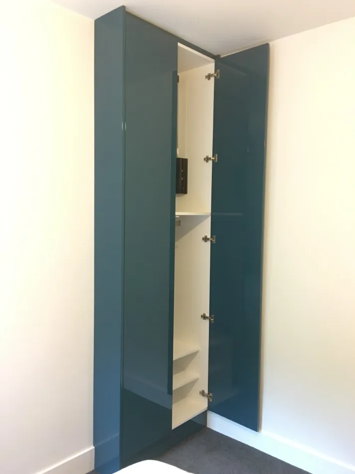 Tall corner cabinet with glossy dark teal doors, one door open revealing white interior shelves.