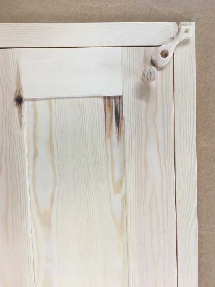 Unfinished wooden cabinet door panel with a loose wooden knob and handle resting on top.