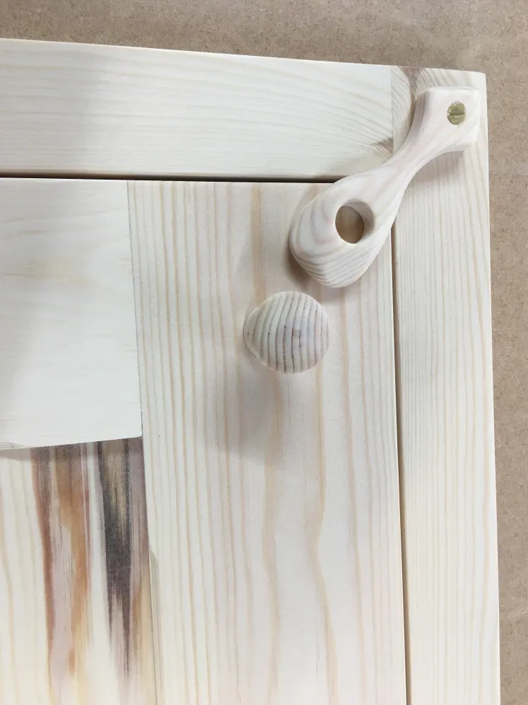 Light wood shaker cabinet door with embedded wooden round knob and a matching wooden latch handle with a circular hole.