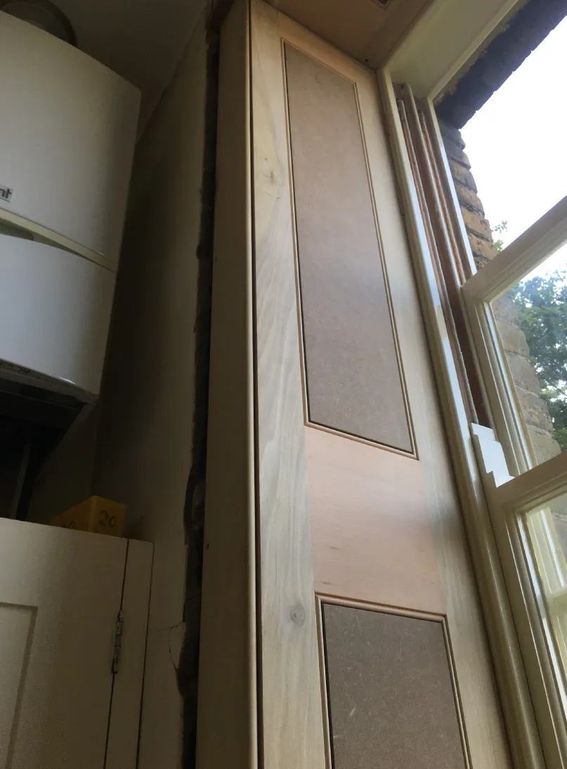 Close-up of a wooden interior window shutter panel partially open, showing the window frame and outside brick wall.