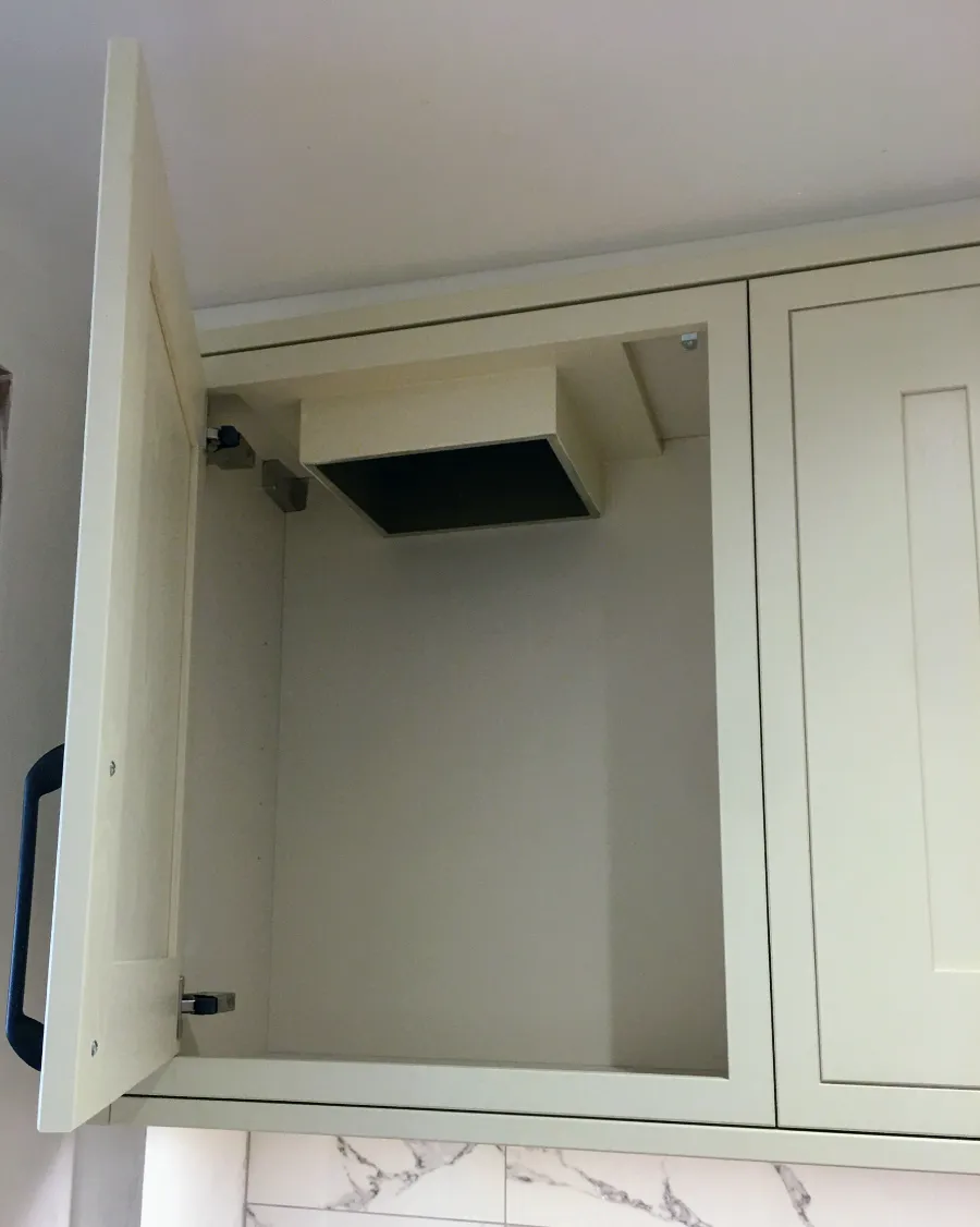 Open empty cream kitchen cabinet mounted on a wall above a marble backsplash.