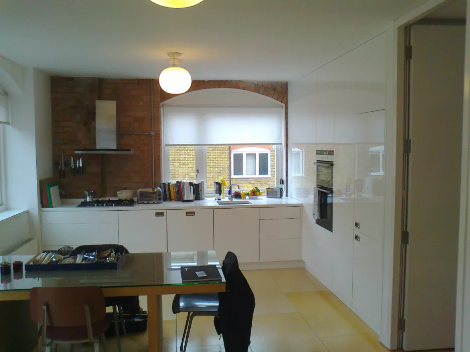 Modern kitchen with white cabinetry, brick accent wall, stainless steel oven, and dining table with chairs in foreground.
