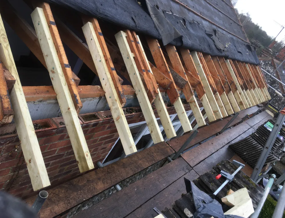 Roof under construction with new wooden battens being installed over old roof structure and black roofing felt partially covering the top.