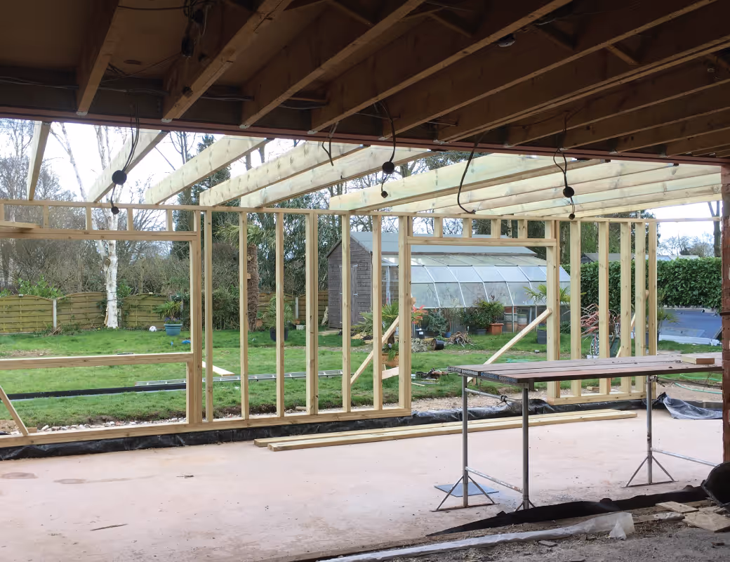 Worker in beige pants and maroon sweater installing drainage system along a building's brick foundation wall.