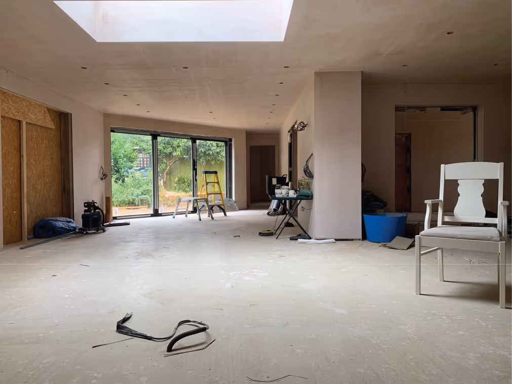 Worker in beige pants and maroon sweater installing drainage system along a building's brick foundation wall.