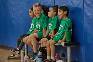 Kids sitting in the Circle City Center gym on a bench with their sports unforms laughing and talking.