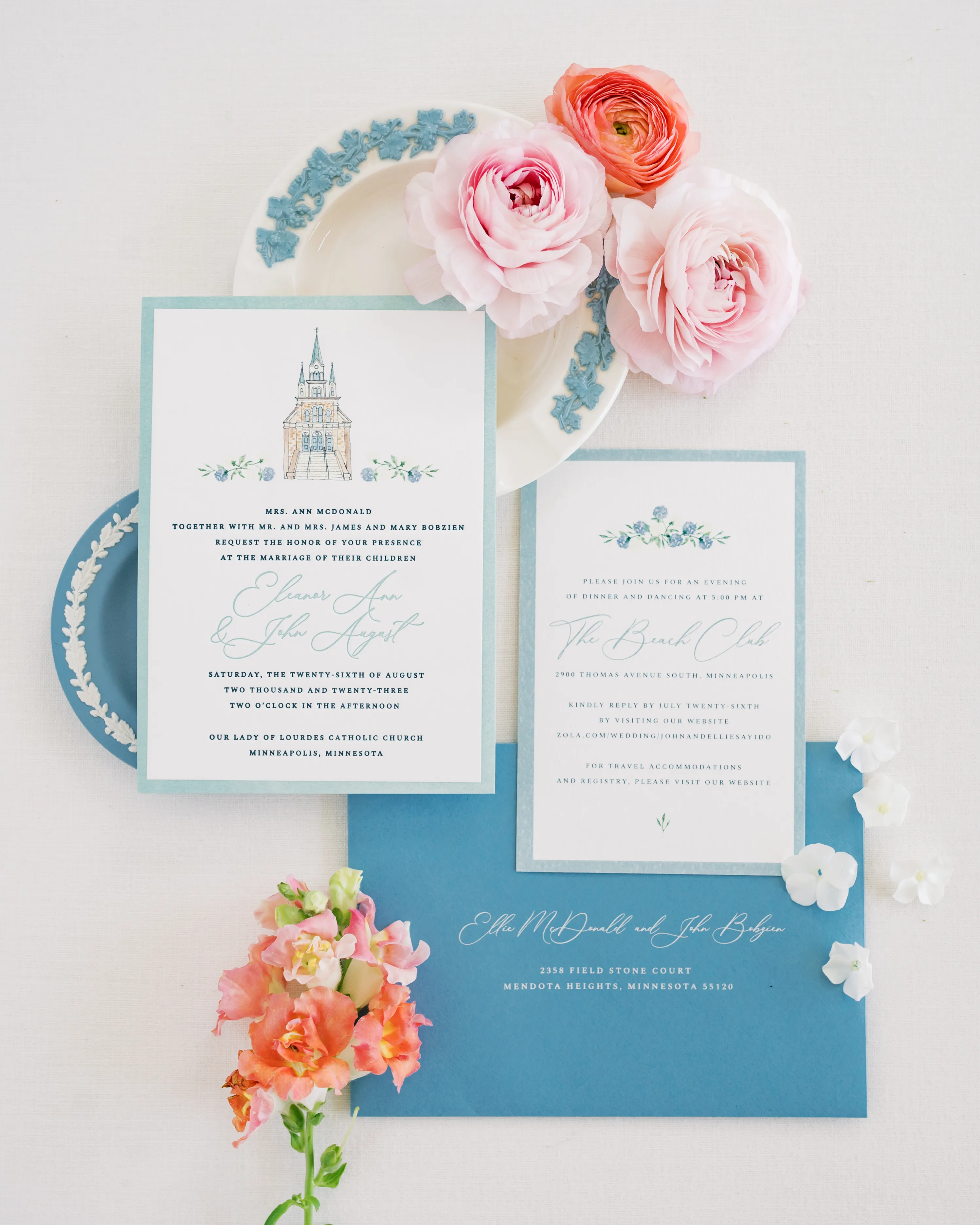 Elegant wedding invitation suite with pastel flowers, blue envelope, and decorative plates on white background.