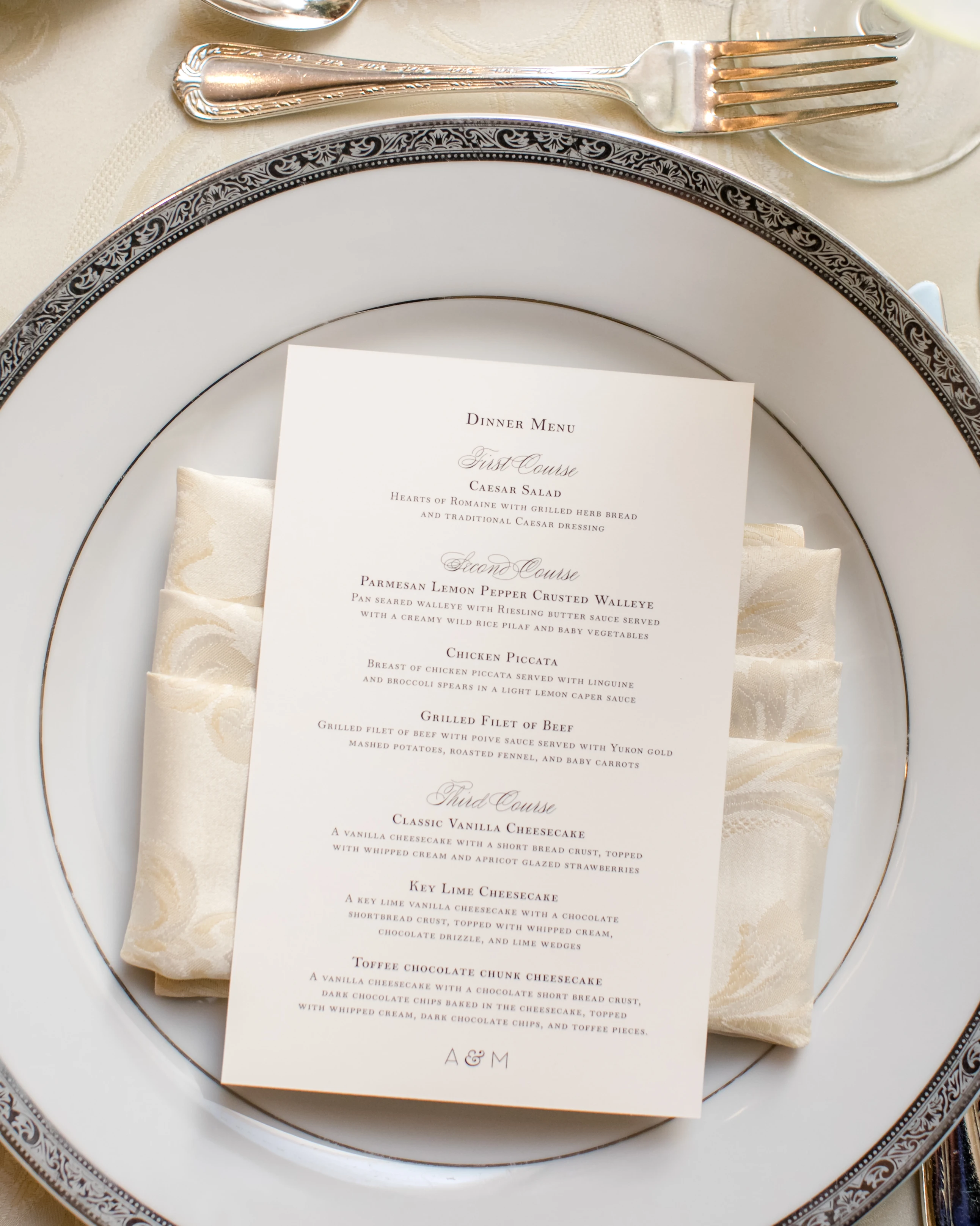 Elegant dinner menu on a patterned plate with cream-colored napkin and silver fork and spoon.