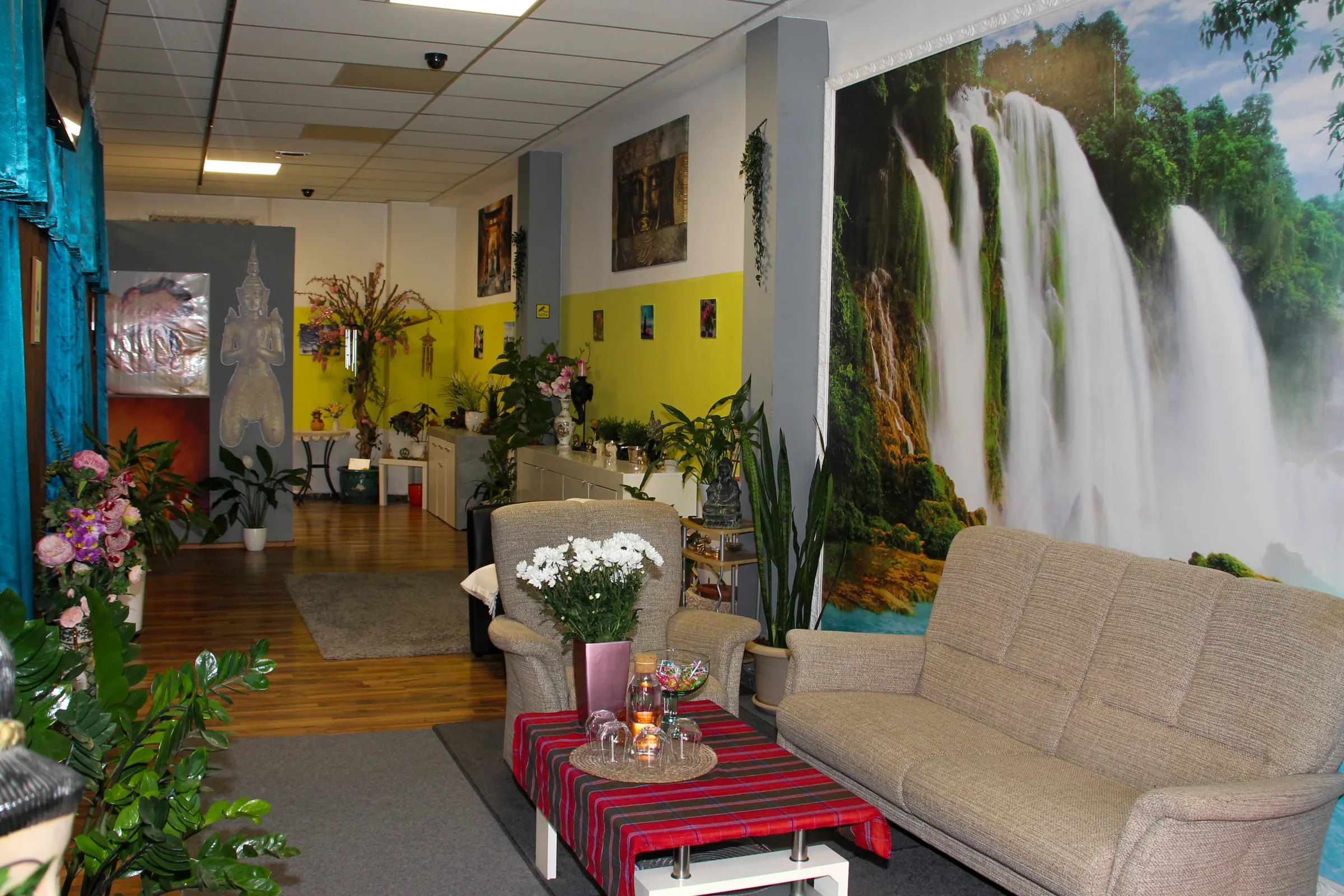 Wartebereich mit Sofas, Blumen und Wasserfall-Wandbild im Thai-Massage-Salon Kelheim