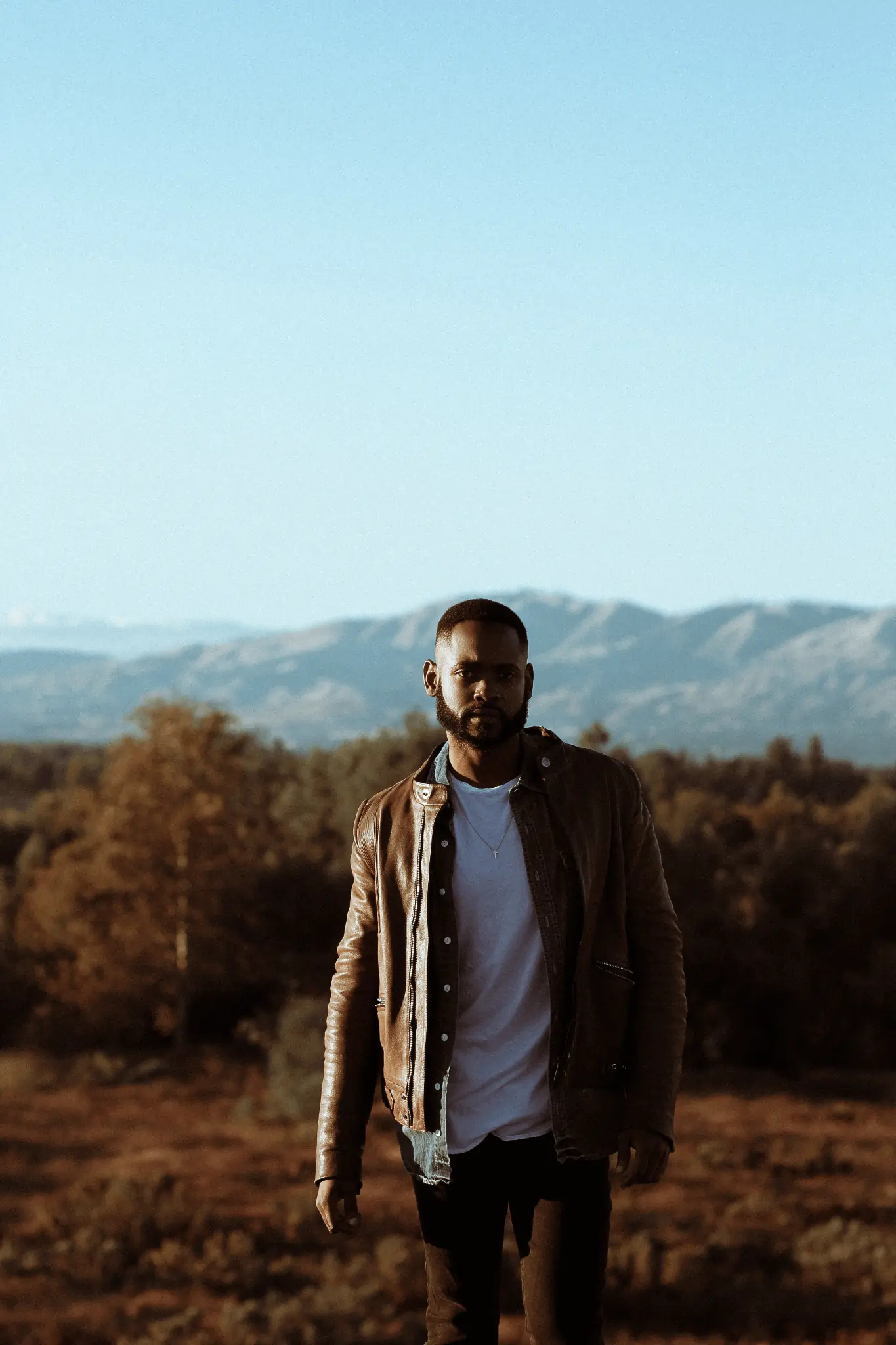 a man standing in a field with mountains in the background