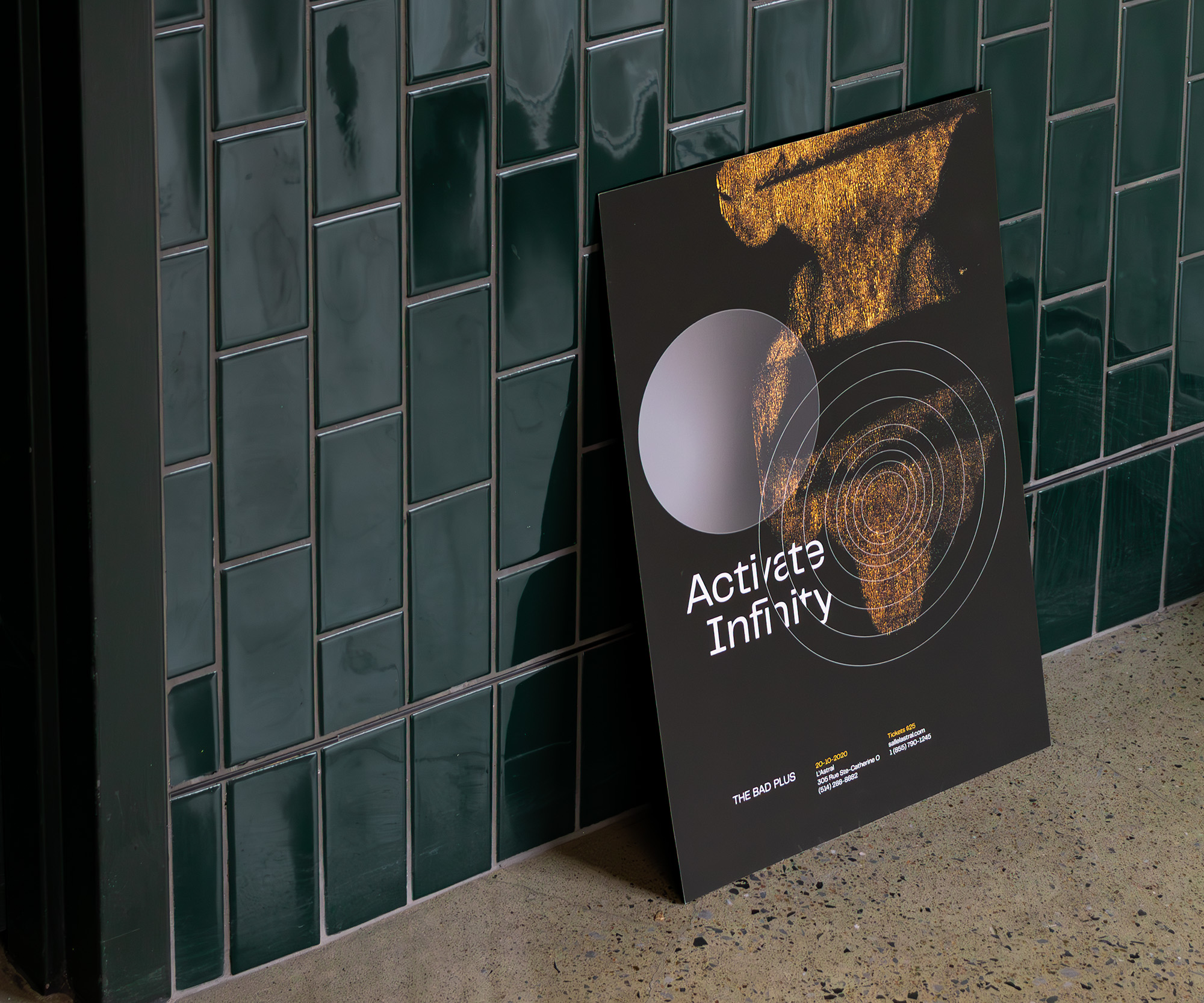 Poster leaning at the base of a glossy tiled wall advertising a performance from The Bad Plus at L’Astral. The same pitted texture is present at the top of the poster, accompanied by seven concentric circles intersecting with the album name on a black background. Concert details are listed at the bottom.
