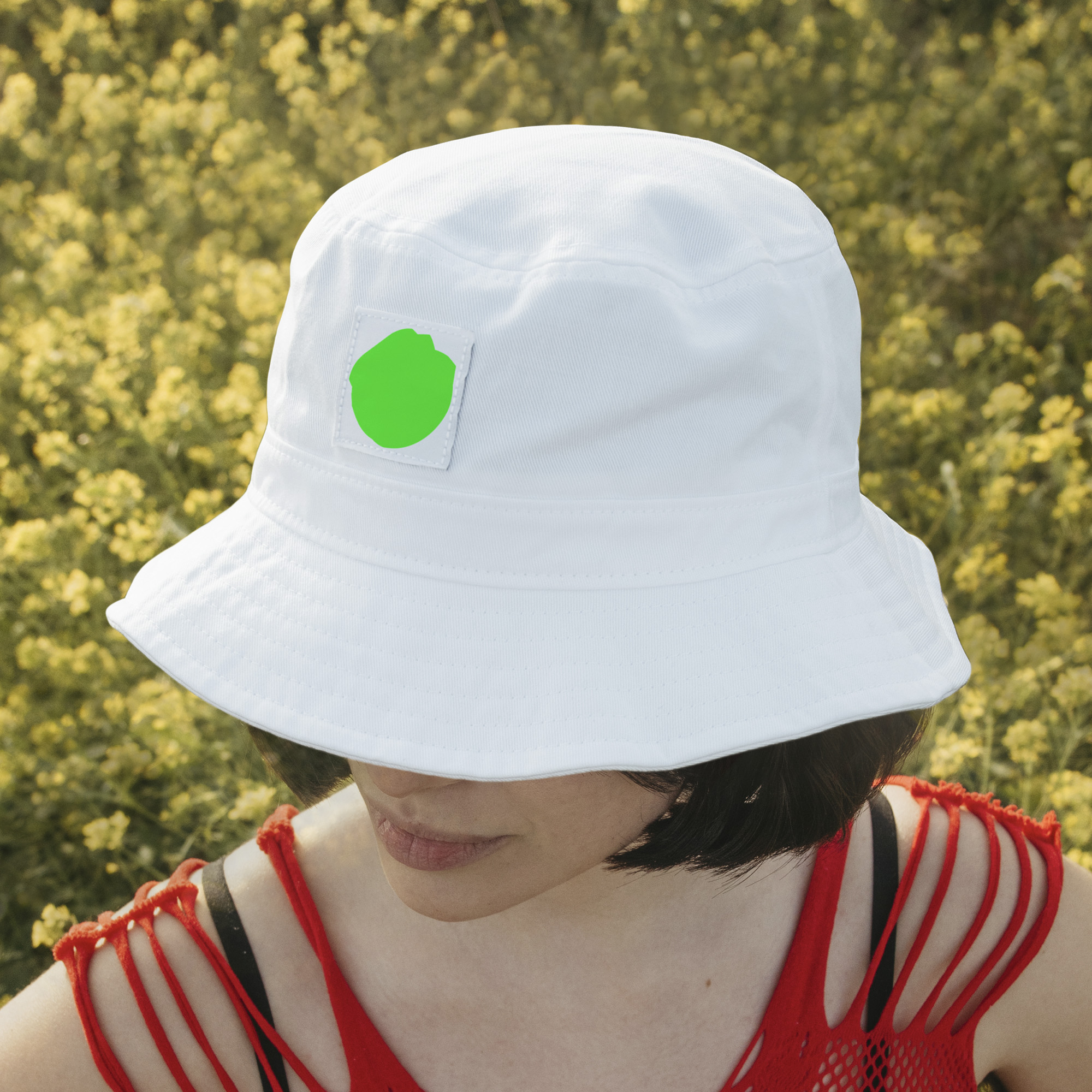 A person wearing a white bucket hat with a rounded, asymmetrical, fluorescent green shape printed on the front.