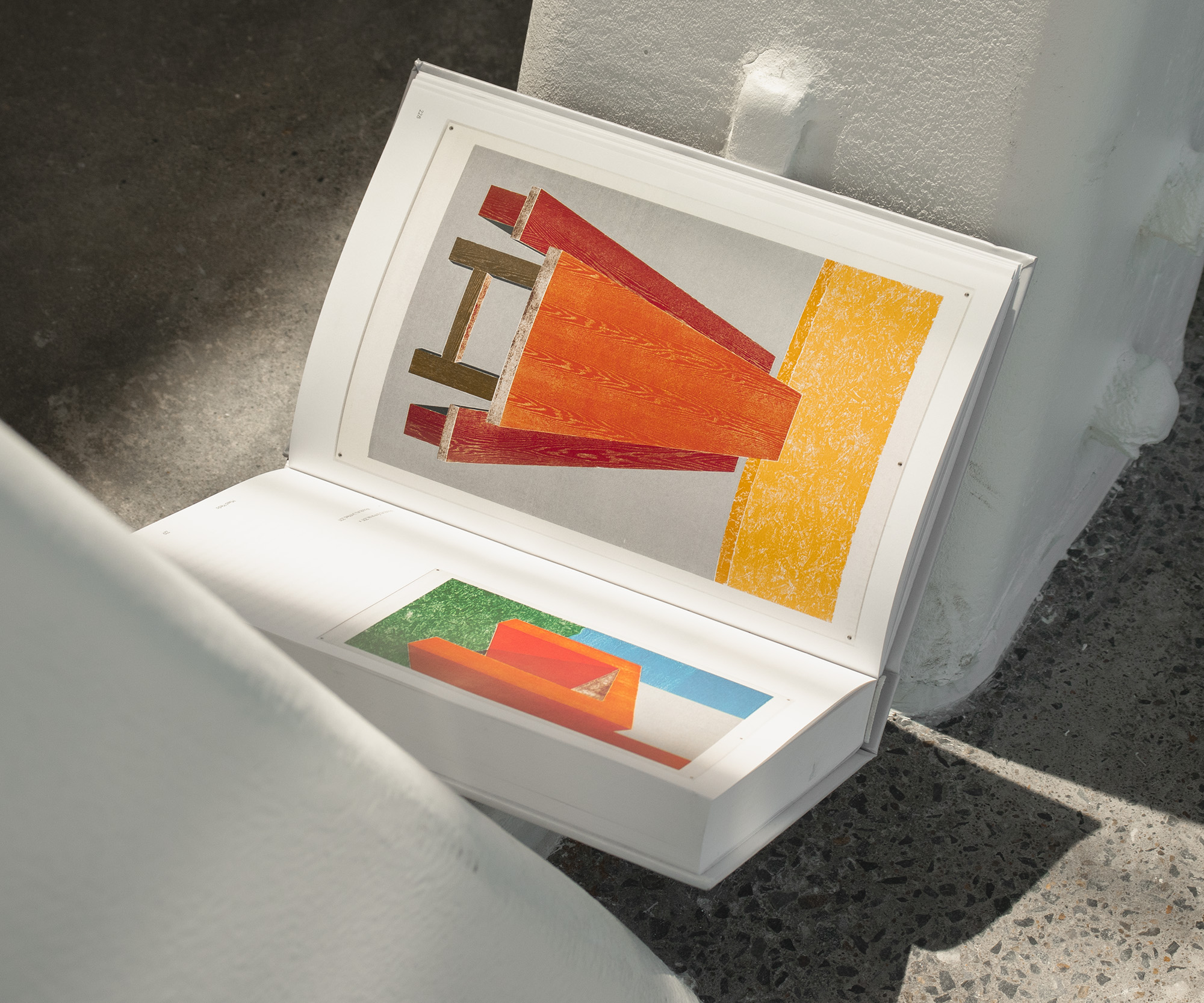 A book lying open at the base of two angled metal beams. Two artworks are visible; both from Thomas Schütte’s 2011 “Untitled from Woodcuts”.