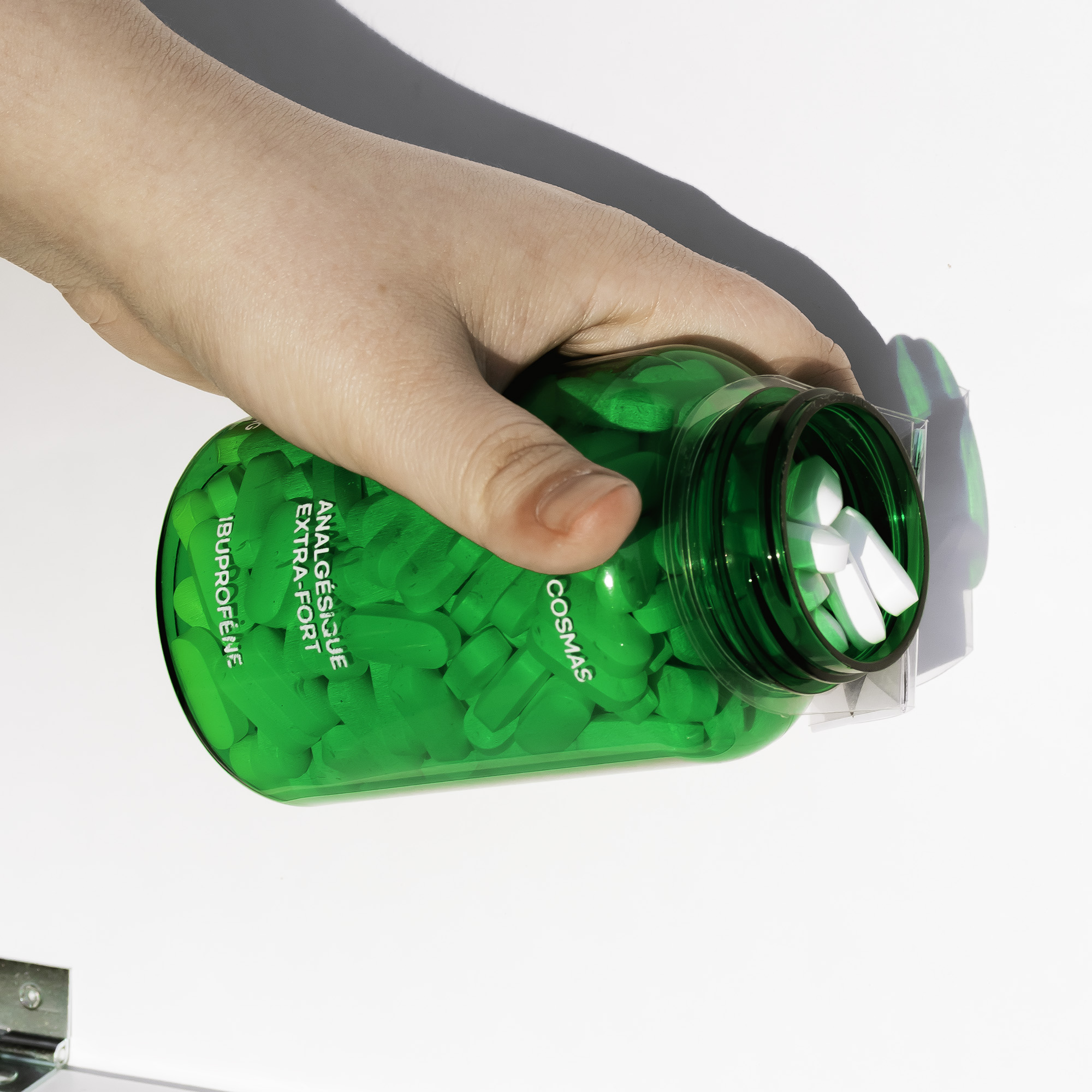 A hand tilting an open pill bottle over a white background. French text on the bottle reads «Analgésique Extra-Fort» and «Ibuprofène».