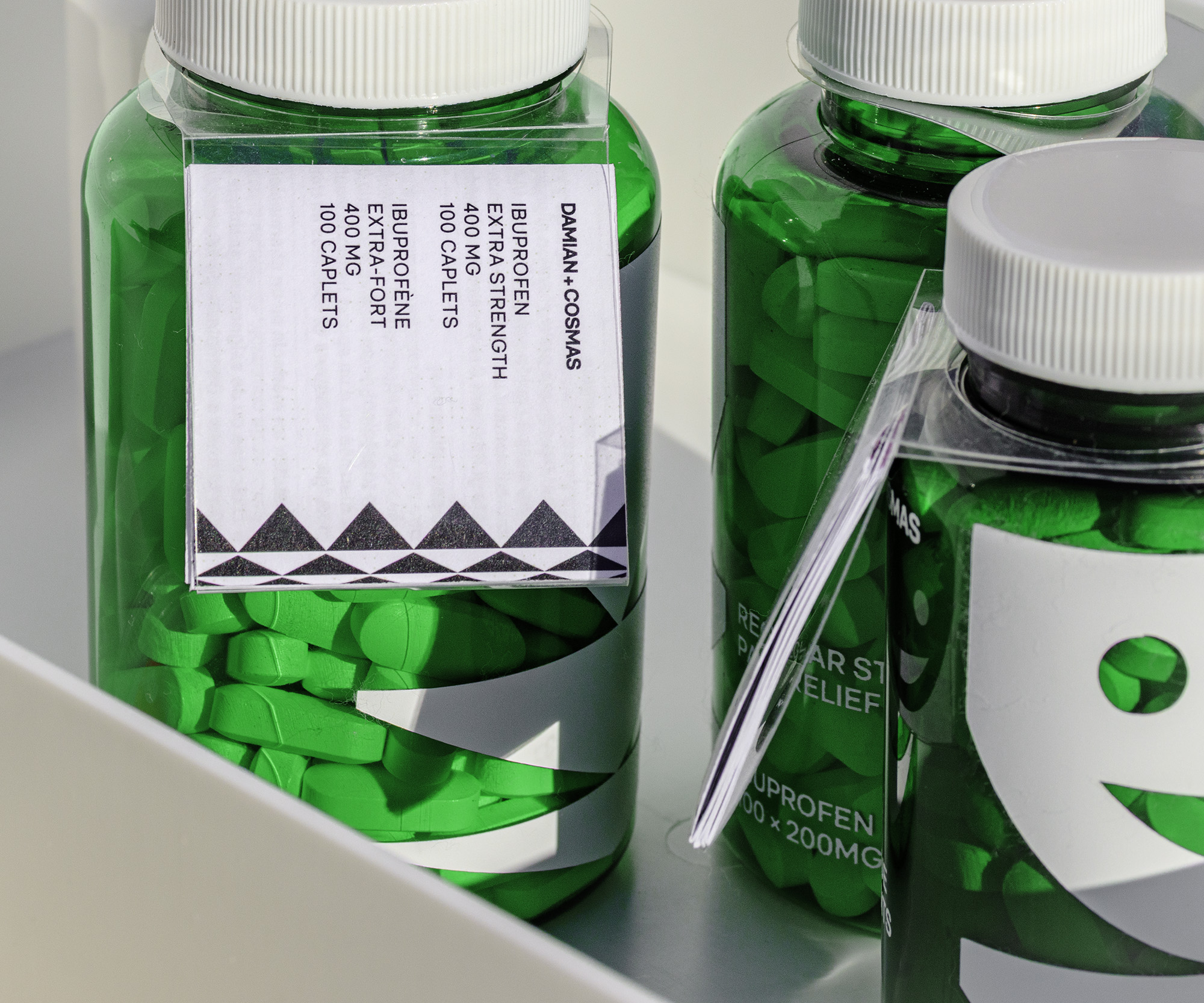 Close shot of the three pill bottles featuring the leftmost bottle’s tag, which lists the quantity and strength of the Ibuprofen it contains. 