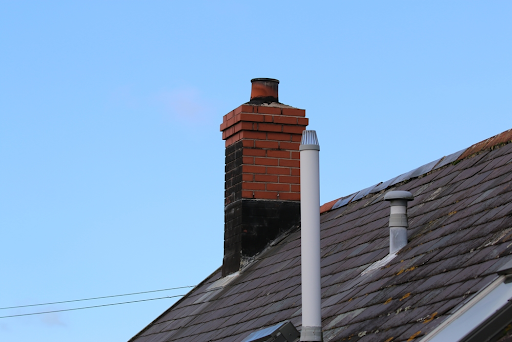 Slate roof with a brick chimney, a tall white soil vent pipe and a smaller vent cap