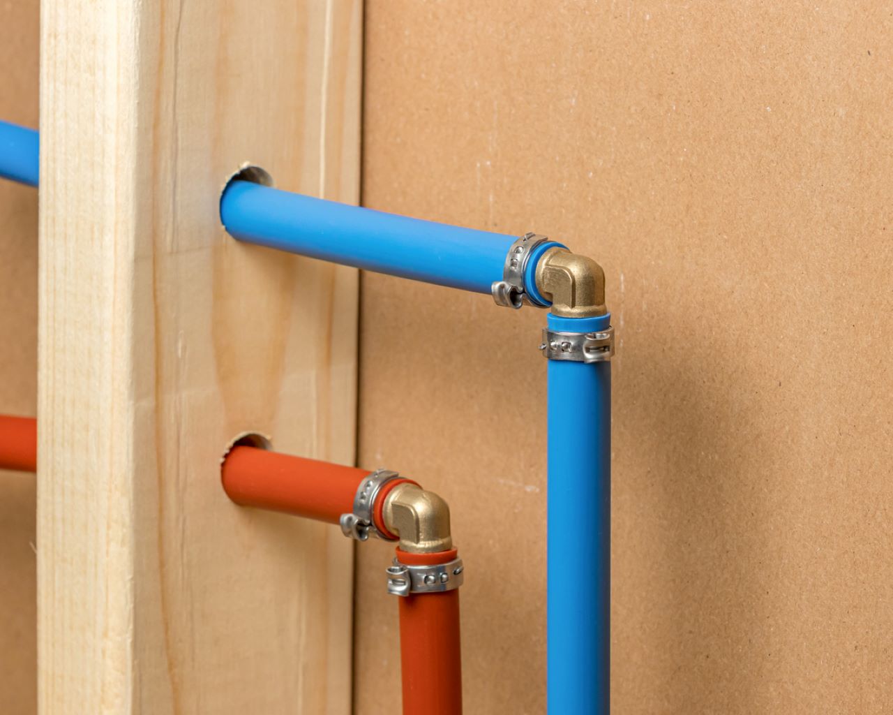 Blue and red plastic pipes with brass elbow fittings running through a timber stud wall