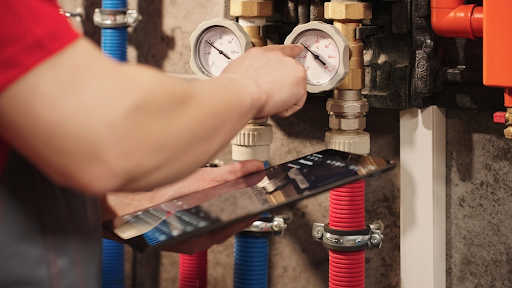 Engineer checking pressure gauges on heating pipework while holding a tablet