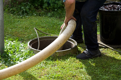 Worker lowering a wide suction hose into an open round tank lid set in a lawn
