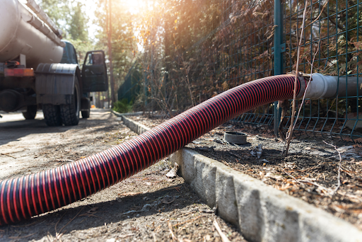 Red and black suction hose running from a tanker lorry to a pipe by a fence
