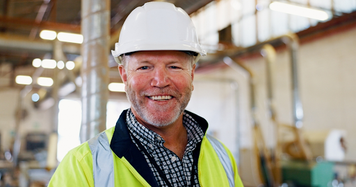 Smiling worker in a white hard hat and hi-vis jacket inside an industrial building