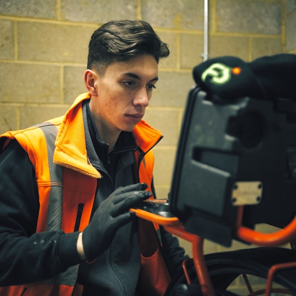 Worker in a hi-vis vest looking at the screen of a drain camera unit