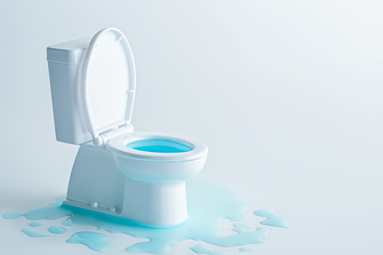 White toilet with the lid up and blue water spilling over onto the floor around it