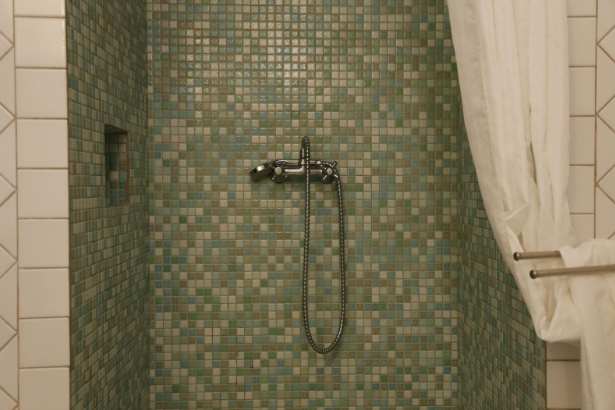 Shower with green mosaic tiles, a wall-mounted mixer and hose, and a white curtain pulled aside