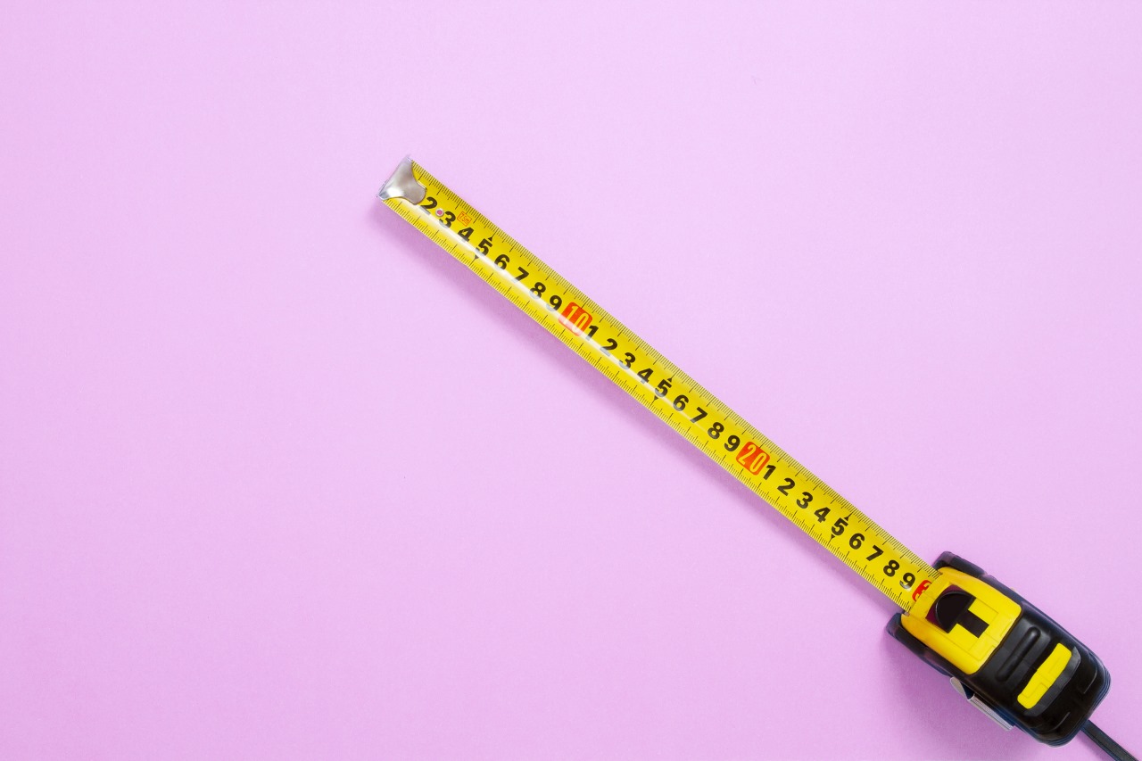 Yellow tape measure extended diagonally across a plain pink background