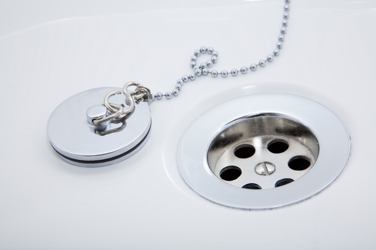 Chrome plug on a ball chain beside an open basin waste in a white sink