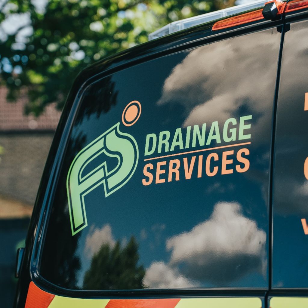 Dark van window with a green and orange drainage services logo reflecting clouds