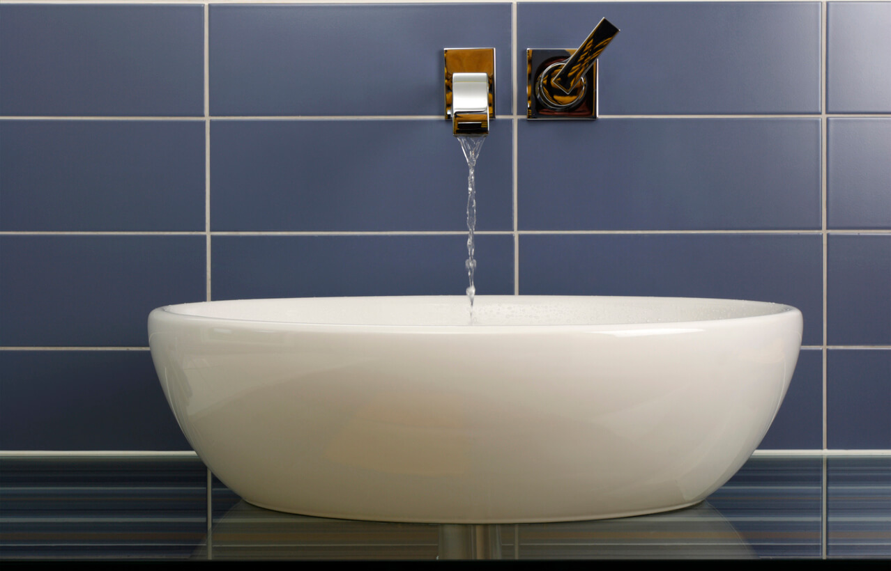 White vessel basin below a wall-mounted chrome tap with water running