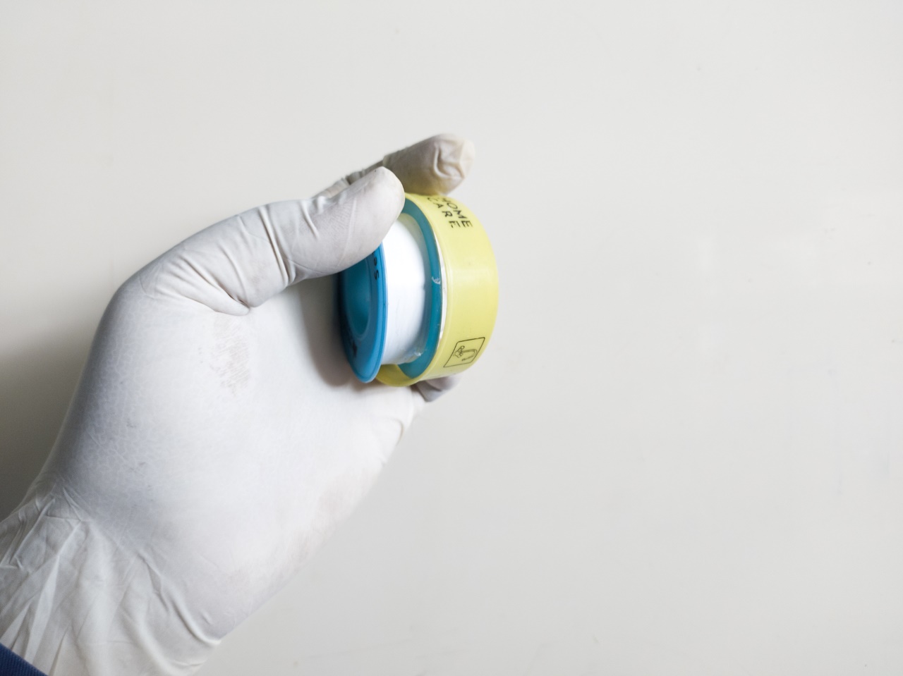Gloved hand holding a roll of white PTFE plumbing tape against a plain background