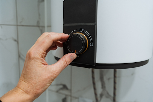 Hand turning the temperature dial on a wall-mounted electric water heater