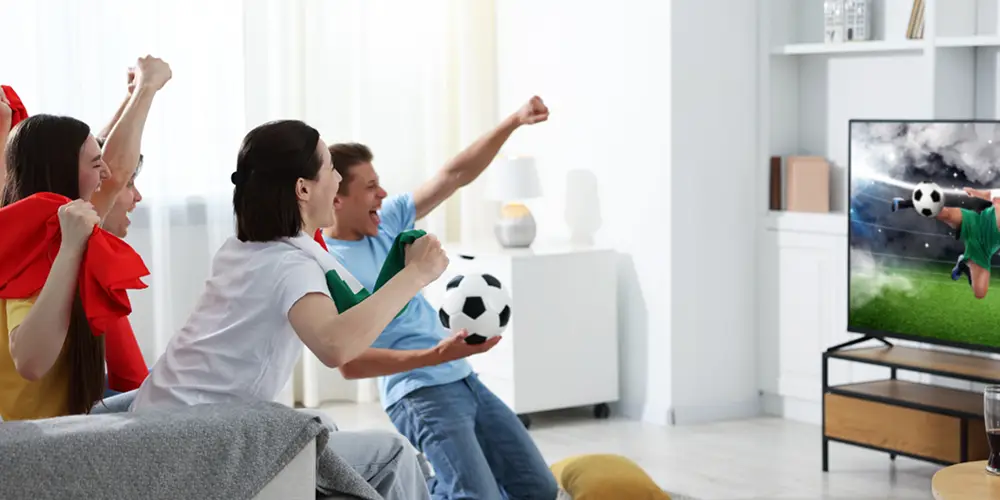 Group of friends cheering while watching a soccer match on TV in a living room.