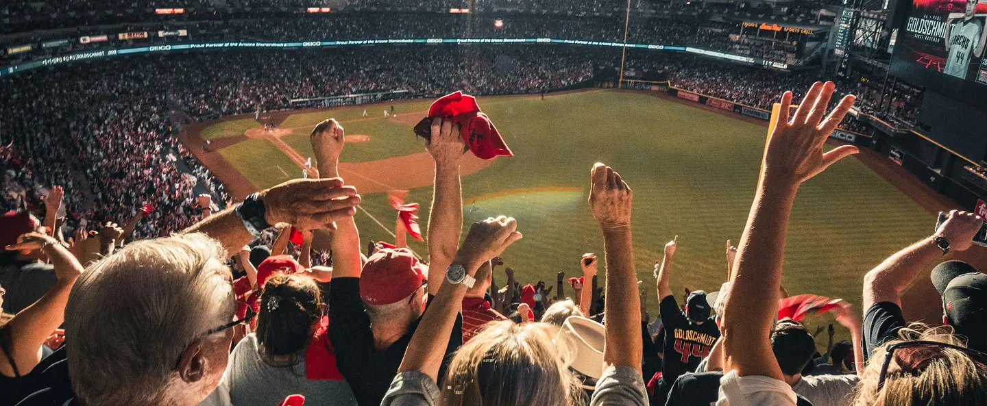 Crowd cheering with raised hands and red rally towels at a baseball stadium during a game.