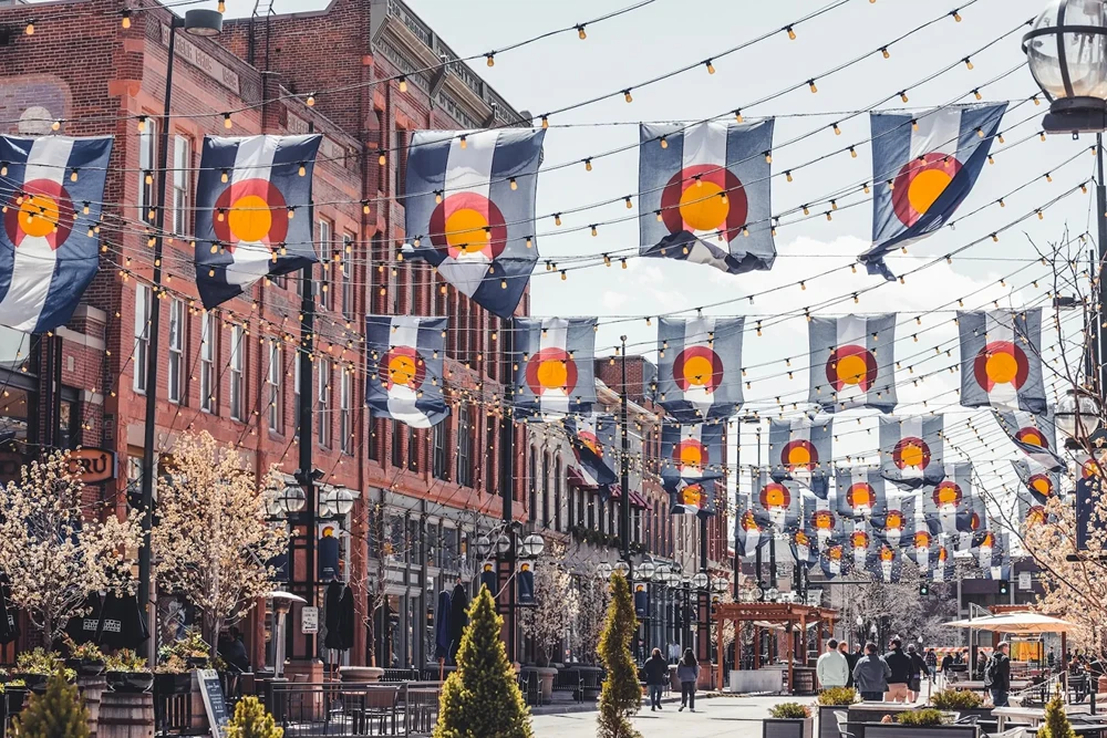 Street decorated with numerous Colorado state flags and string lights on a sunny day.