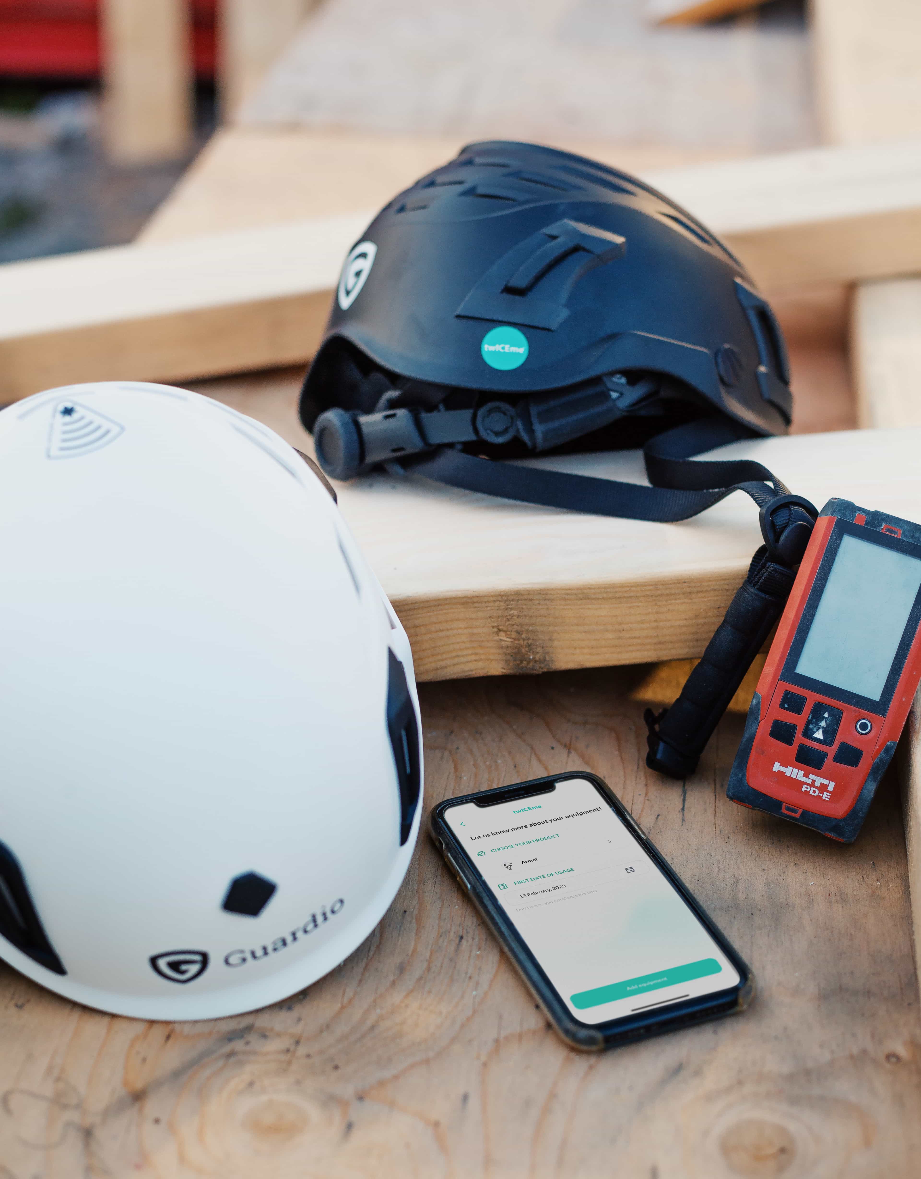 Two construction helmets from Guardio on a table with a phone where the Twiceme app is open