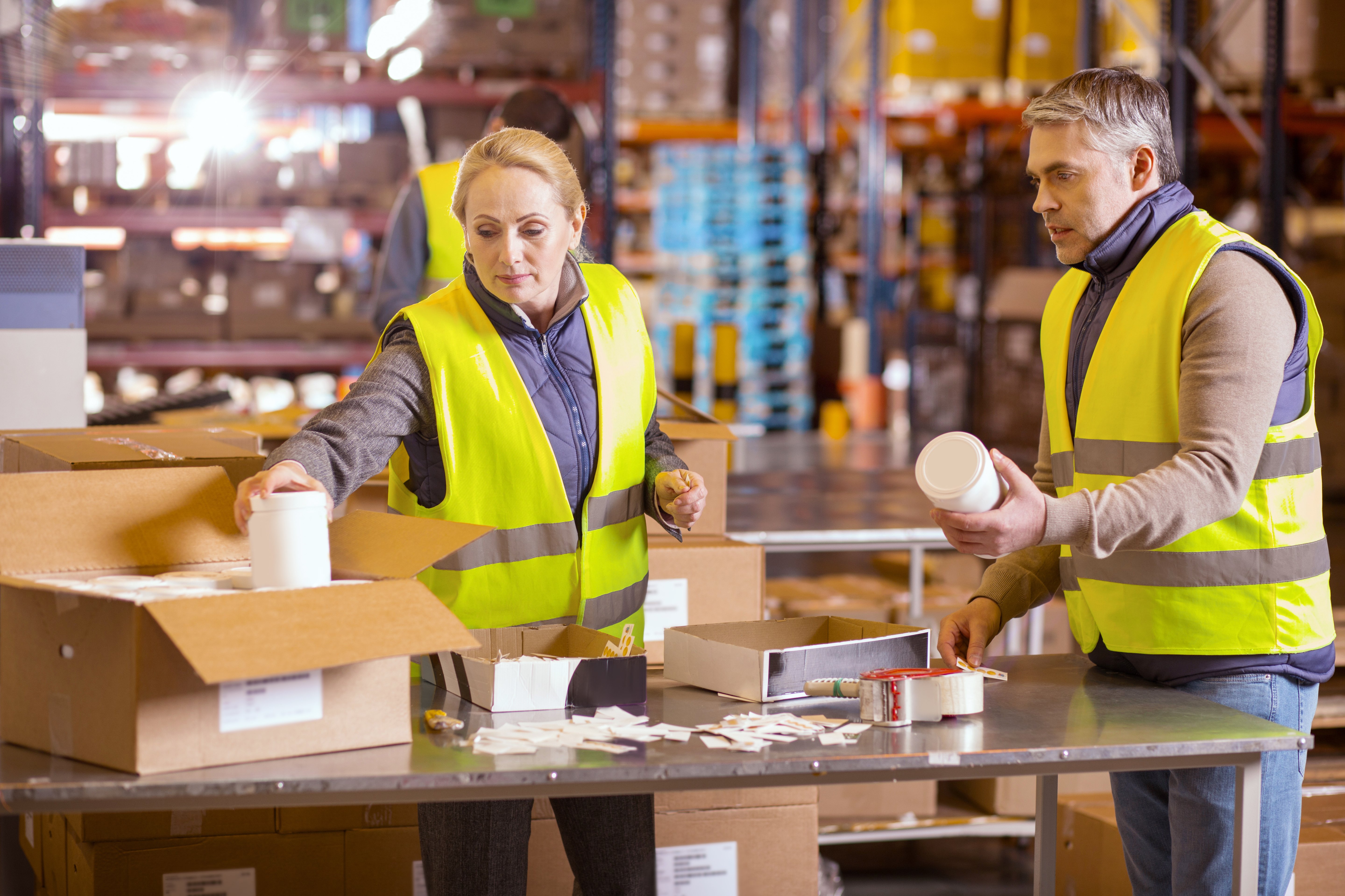 productive male and female warehouse workers packing boxes for shipment at distribution center