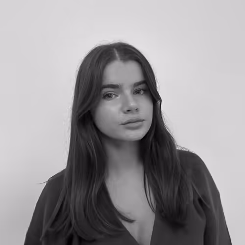Black and white portrait of a young woman with long dark hair wearing a V-neck top against a plain background.
