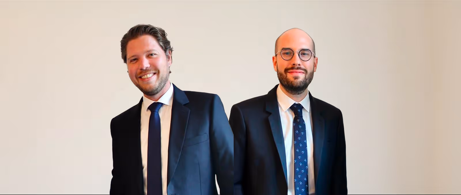 Deux hommes souriants en costume et cravate, l'un avec des lunettes, posant devant un fond beige clair.