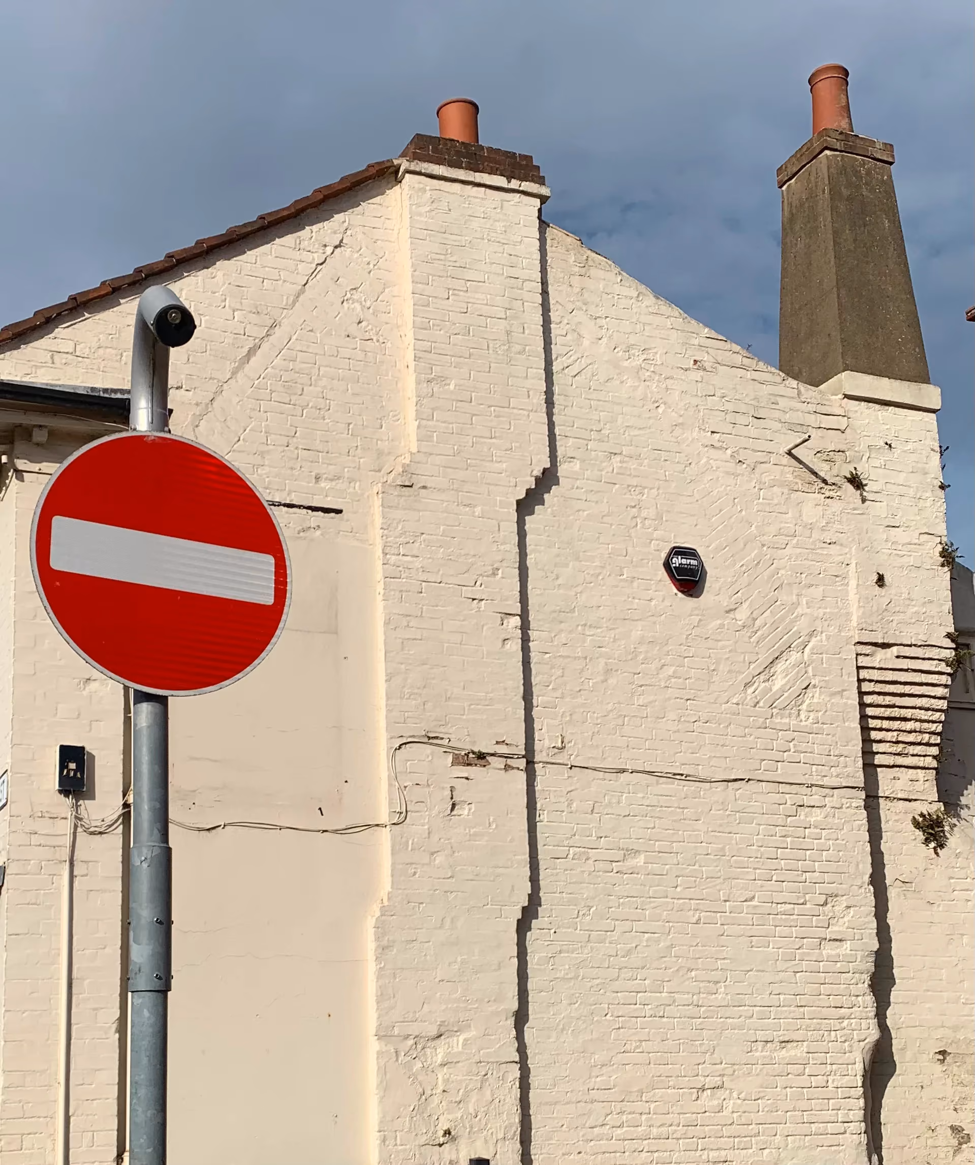 Painted brick gable end behind a no entry sign, with the outline of the earlier steeper roof in the brickwork